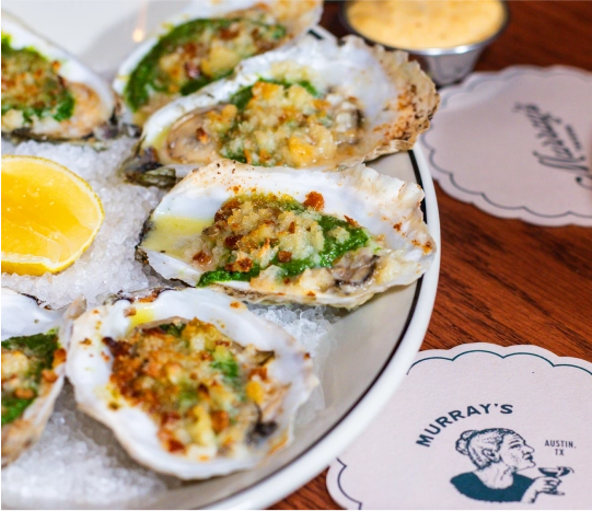 Close-up of several oysters on a plate next to a Murray's-branded coaster.