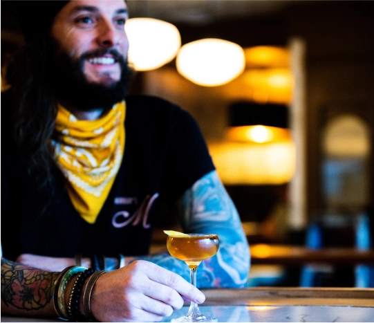 Person sitting behind the bar of Murray's Tavern and smiling, holding a cocktail.